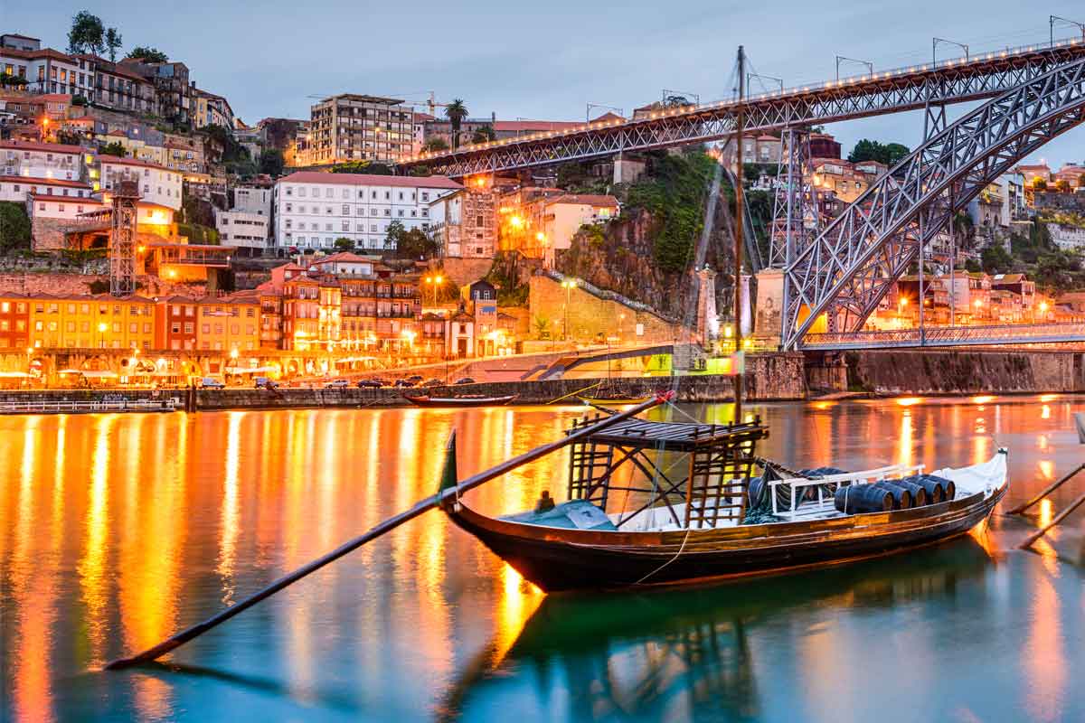 Barca tradizionale ormeggiata nel fiume con il ponte sullo sfondo, illuminata dalle luci della città al tramonto.