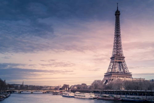 Tour Eiffel se dressant au-dessus de la Seine, avec un ciel nuageux et des bateaux amarrés le long de la rivière.