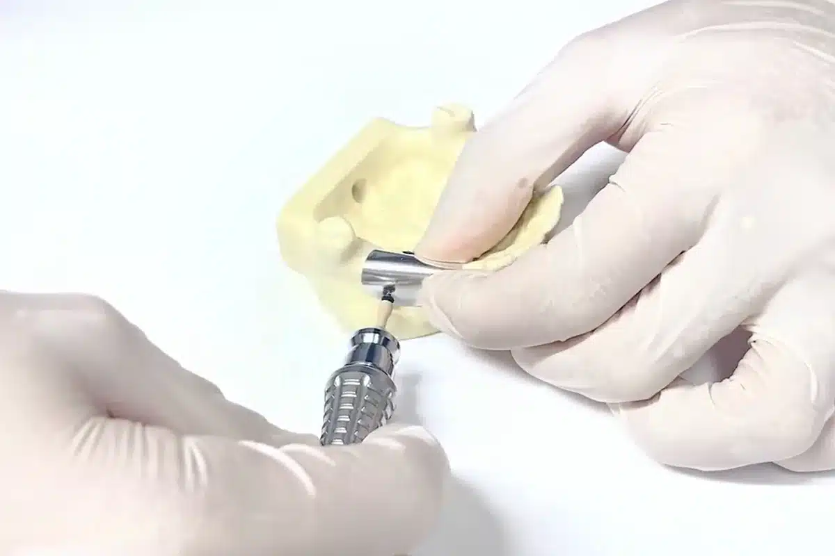 A hand wearing a glove operates a dental tool on a dental model, demonstrating precision in a dental procedure.