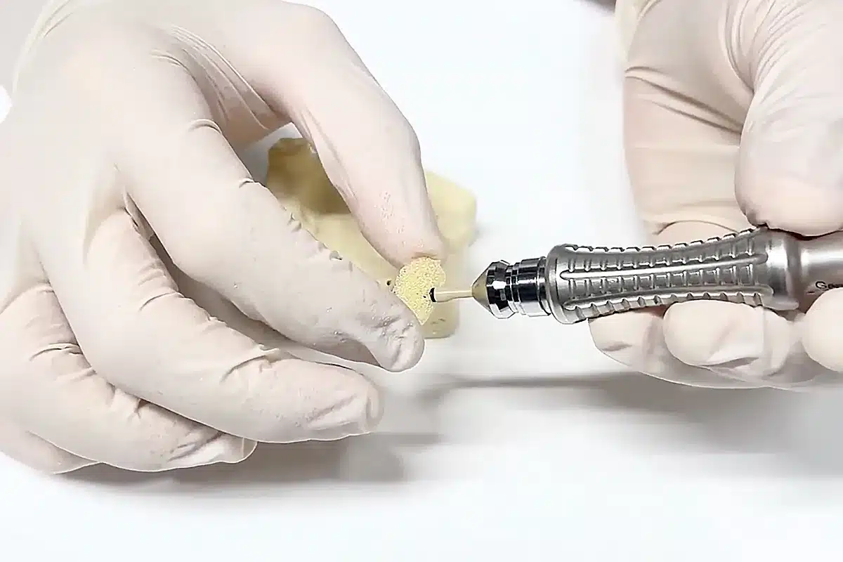 Hand holding a dental drill with a yellow dental model, demonstrating a dental procedure in a clinical setting.