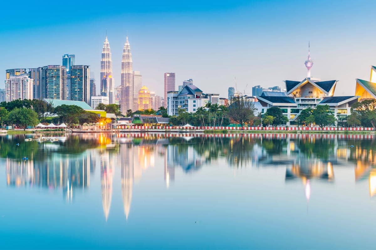 Kuala Lumpur skyline at blue hour with Petronas twin towers reflected in calm lake water, modern buildings and clear sky for large language models.